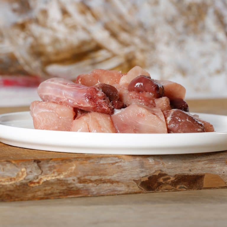 BarfGold alles vom Huhn: Hühnerteile roh, Hälse und Innereien auf einem weißen Teller appetitlich präsentiert.